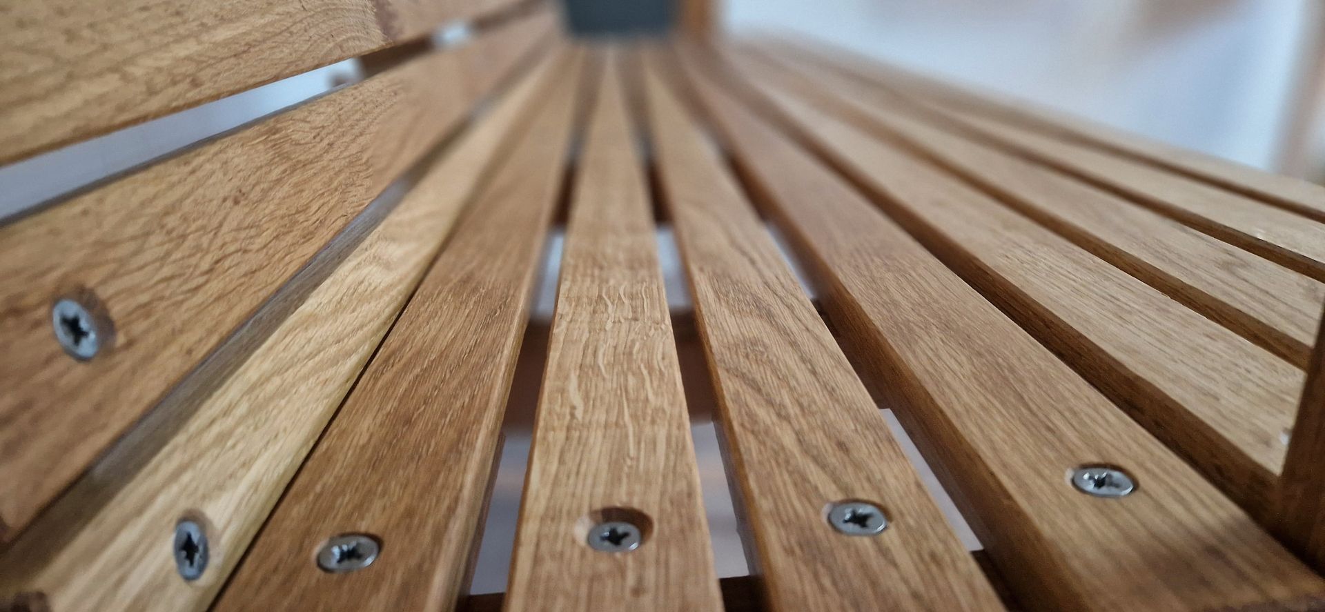 Detailaufnahme einer Holzbank mit schmalen, parallel verlaufenden Holzlatten und verschraubter Konstruktion.