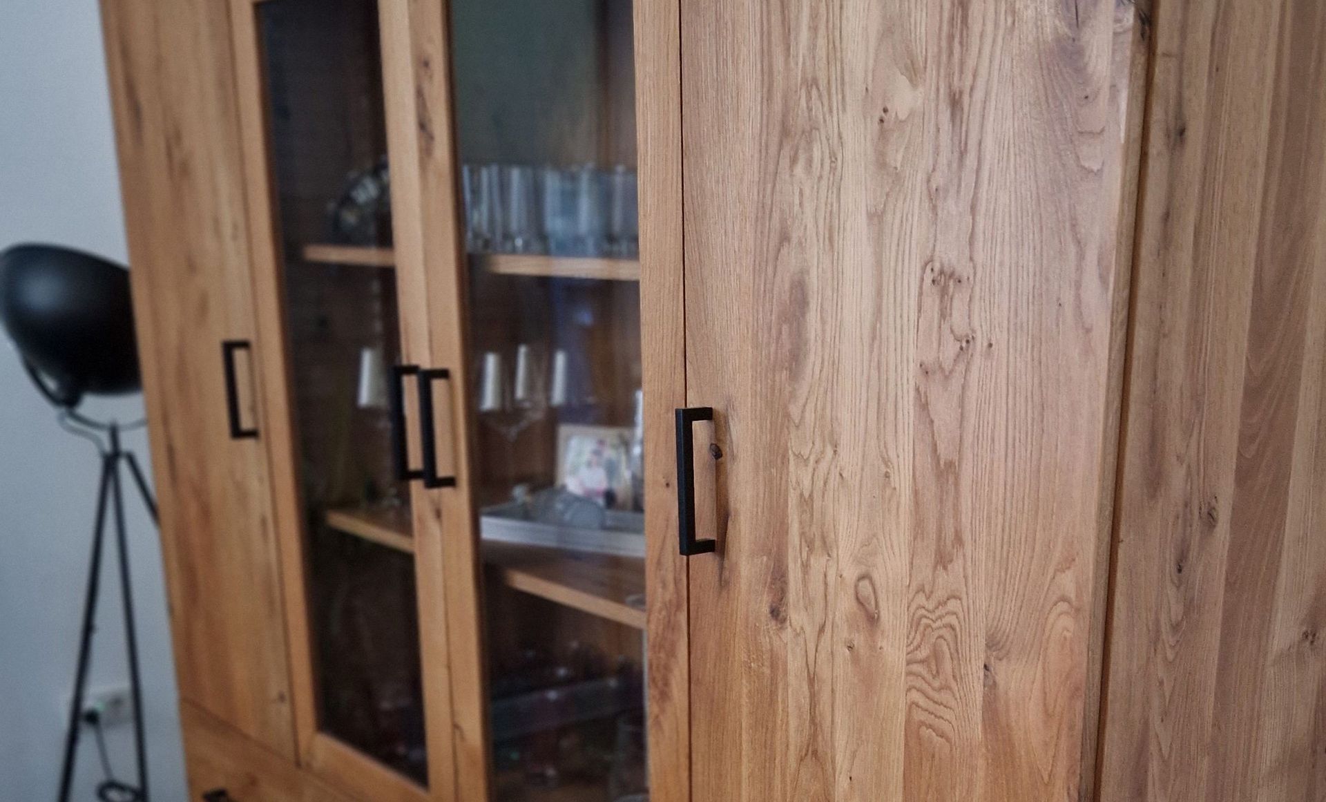 Großer Vitrinenschrank aus Holz mit Glastüren und schwarzen Griffen, gefüllt mit Gläsern und Geschirr.